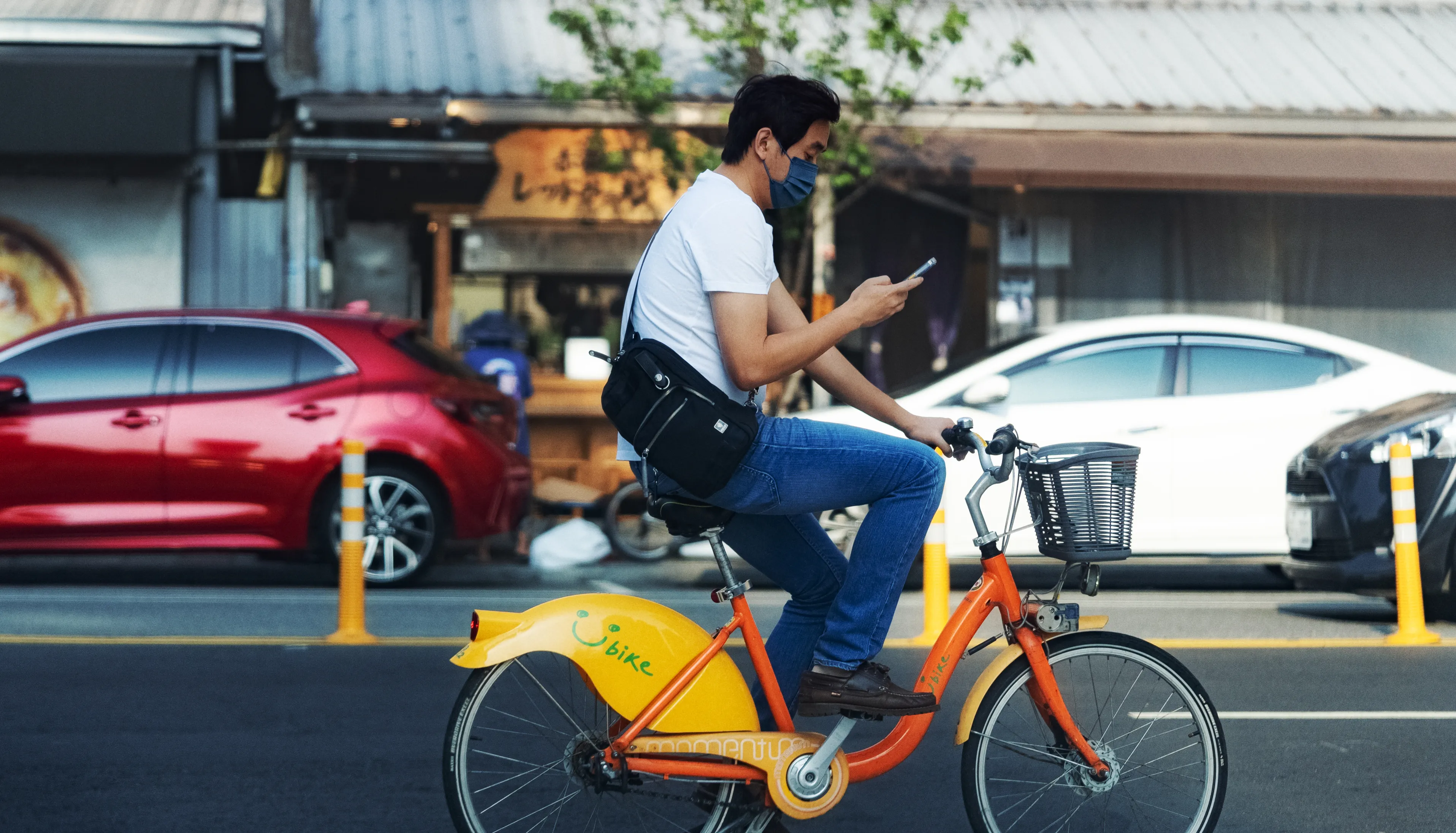 一名人物騎著黃色腳踏車穿過城市道路,身旁有紅色與白色汽車