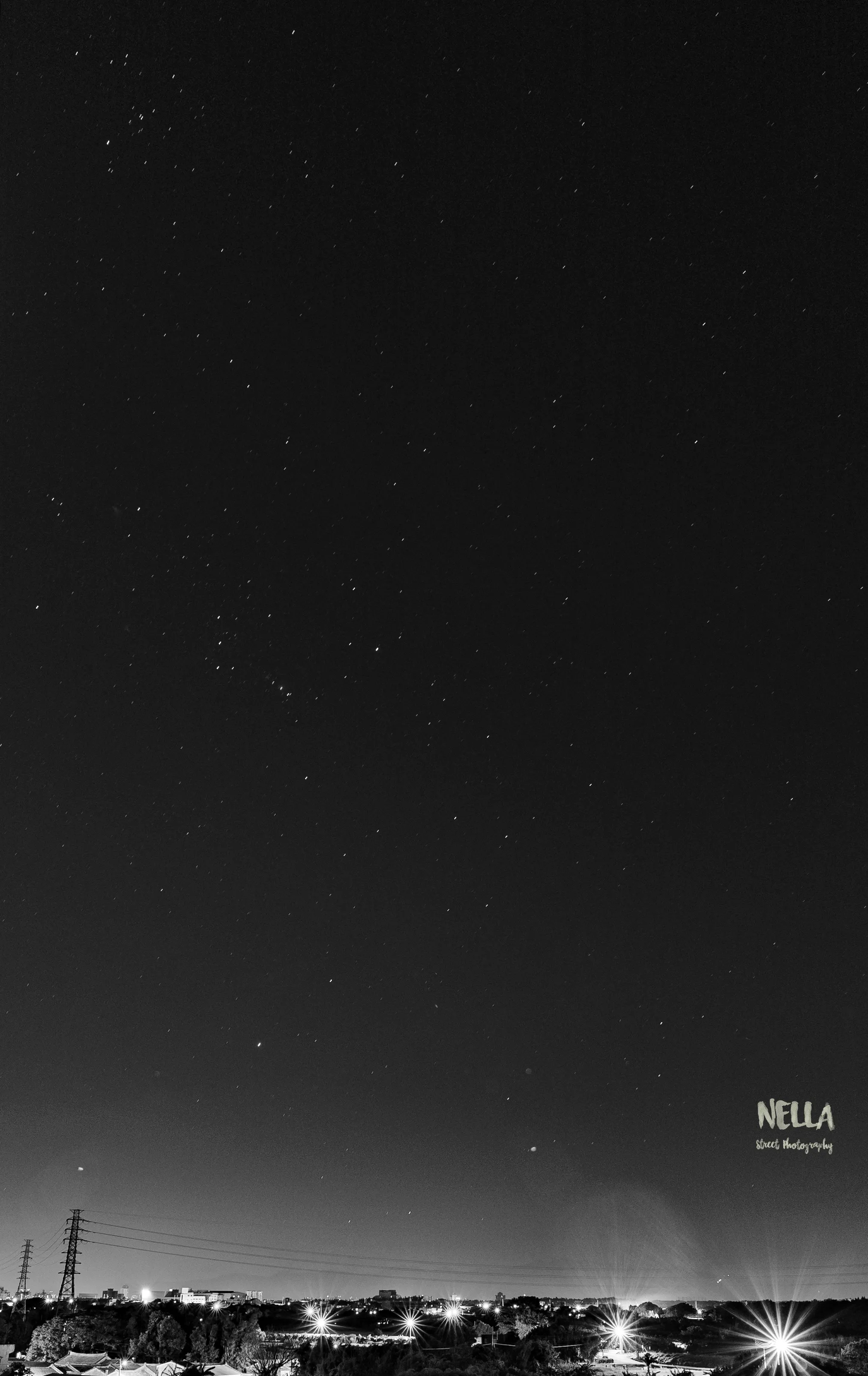稀疏星點布滿深色夜空,下方遠處城市燈火與電塔形成低矮天際線