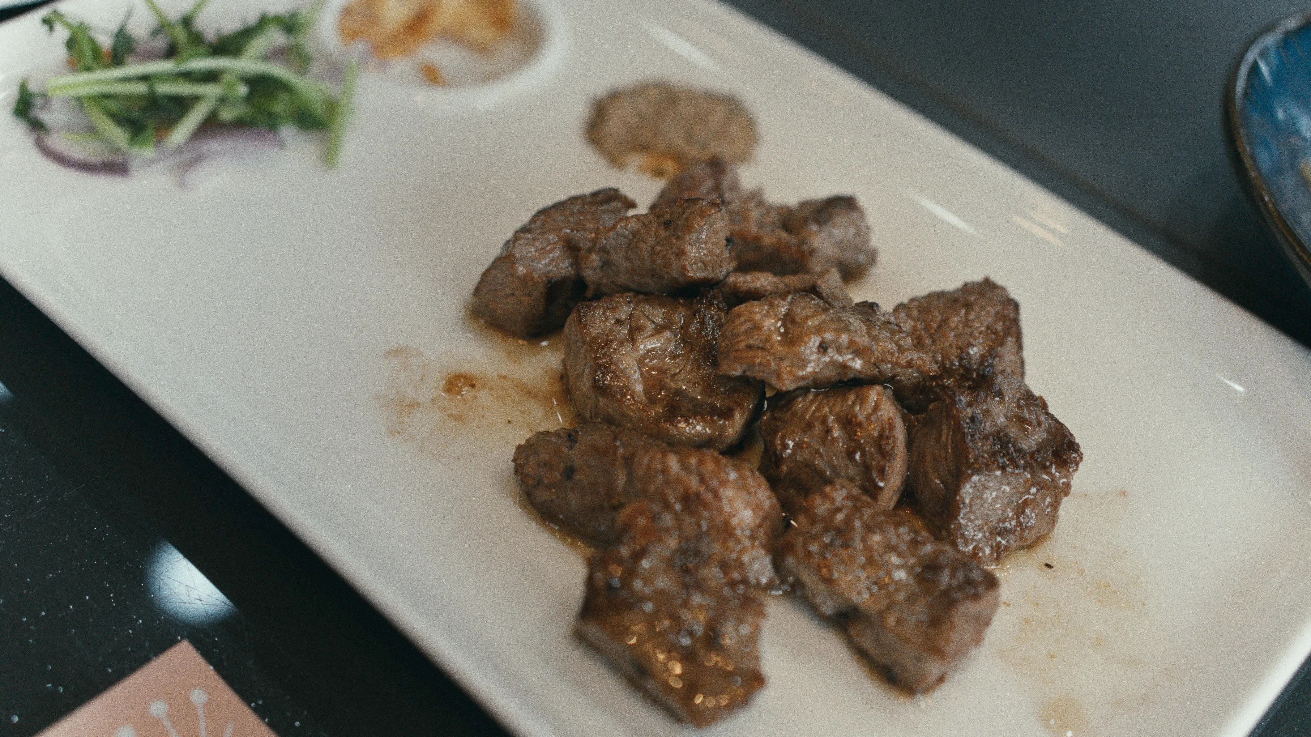 極賞味鐵板燒牛肉丁鐵板特寫，白盤上盛著數塊煎至焦香的牛肉丁，旁邊配生菜與洋蔥絲